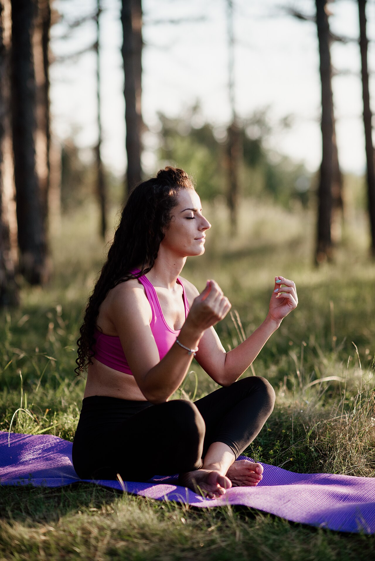 Woman meditating peacefully in a green forest at golden hour